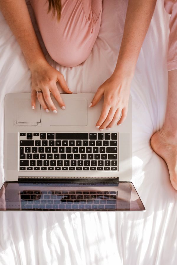 A woman sitting on a bed planning her hen party on the computer