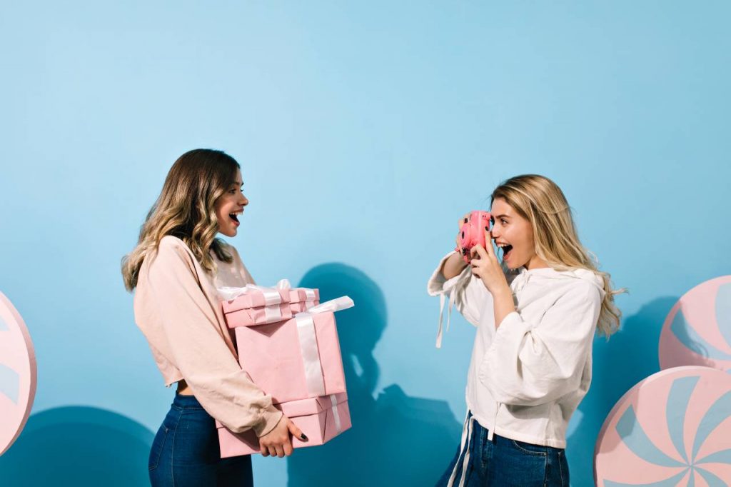 A maid of honour taking a photo of the bride after giving her a gift to invite the bride to her own hen party