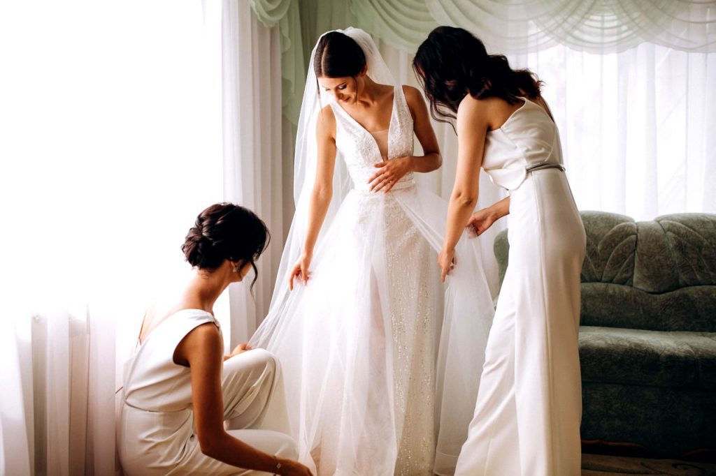 A bride in her wedding dress and two women completing their maid of honour duties