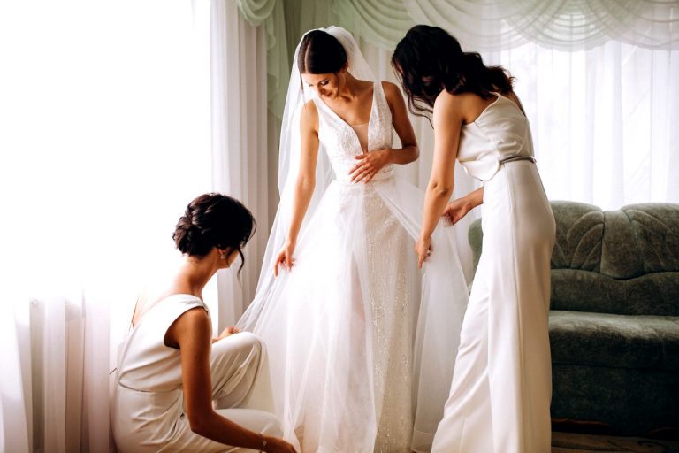 A bride in her wedding dress and two women completing their maid of honour duties