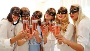 A group of women wearing masquerade masks as their hen party theme ideas and drinking prosecco on their hen do