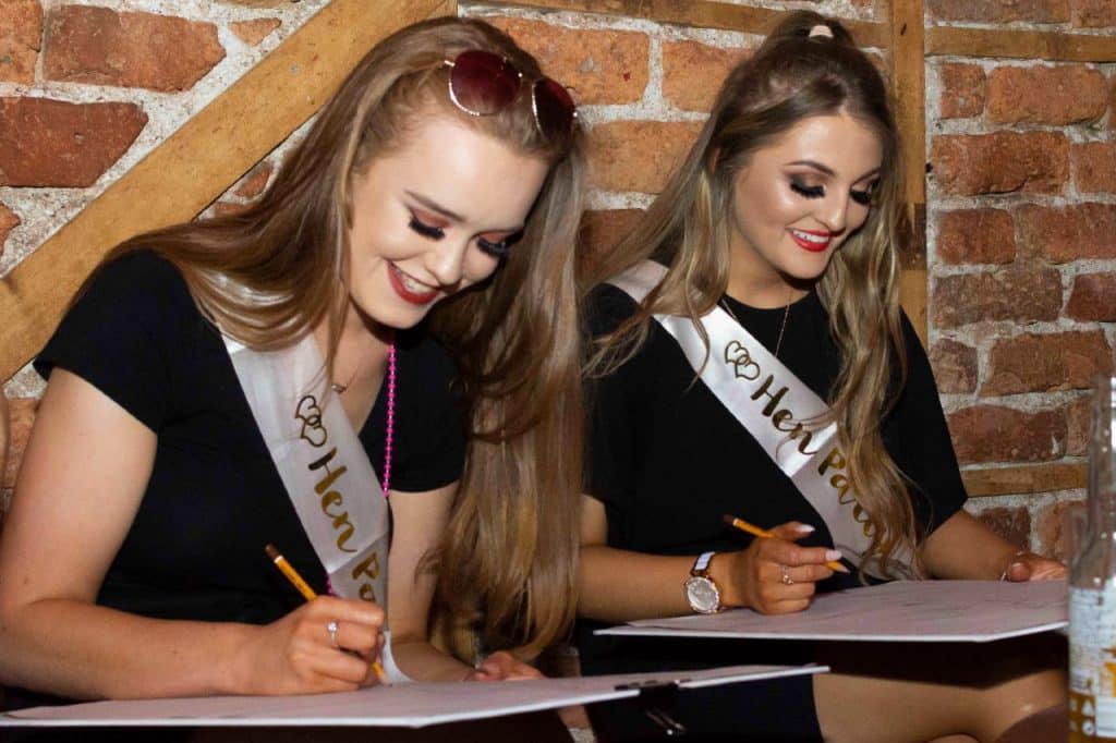 Two girls writing answers for the mr and mrs quiz hen party activity