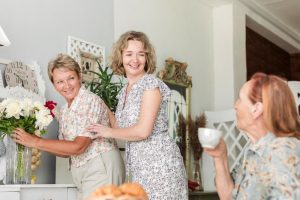 A young woman with two older women in kitchen discussing hen party ideas for mixed ages like an afternoon tea